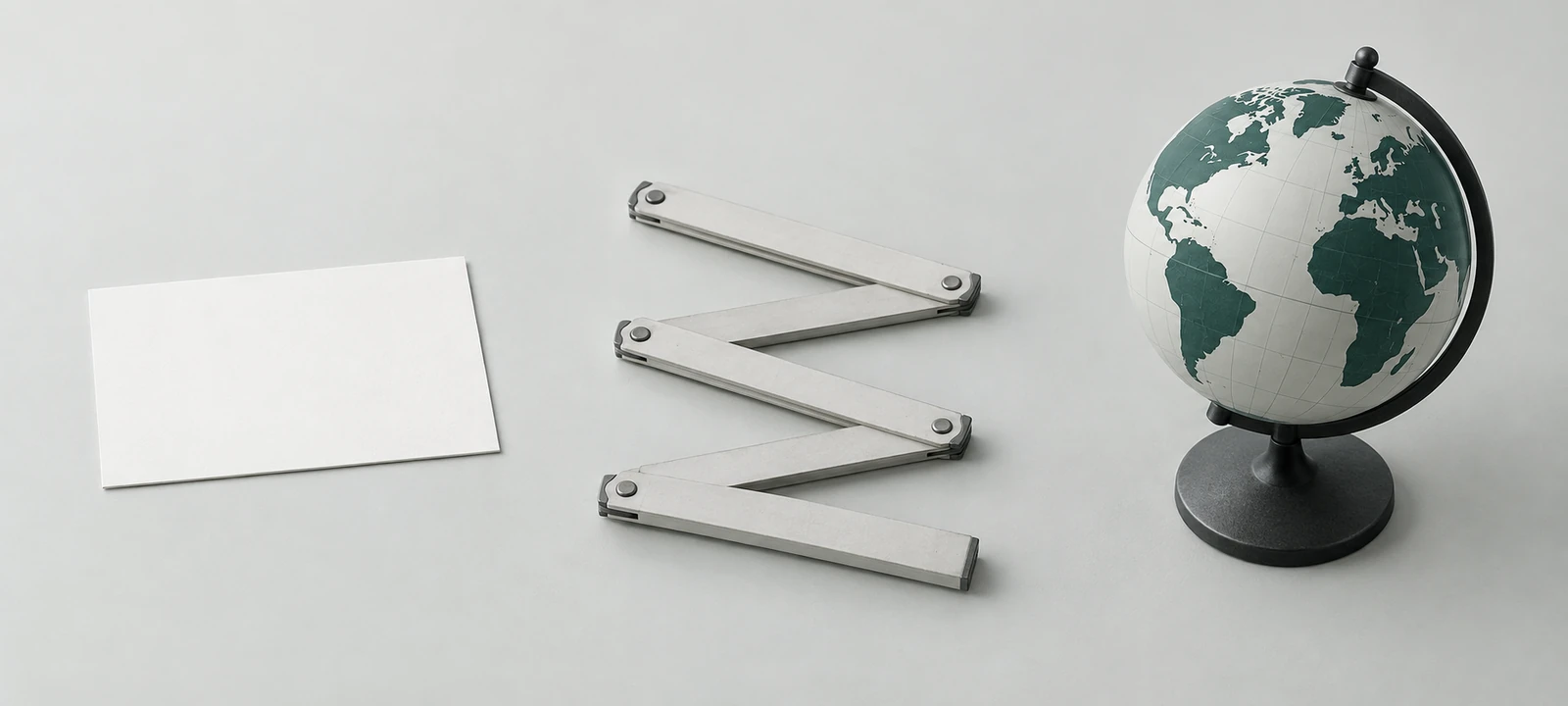Scheda bianca, metro pieghevole e piccolo globo disposti in sequenza su un tavolo. / A blank card, folding ruler and small globe arranged in sequence on a table.